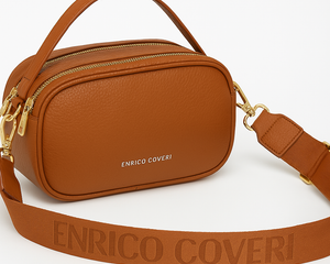 Giovane donna con t-shirt chiara e jeans indossa lateralmente una borsa a tracolla ENRICO COVERI in pelle marrone cognac